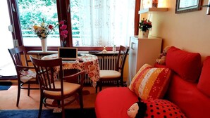 A cozy living room with a red sofa, a wooden dining table with chairs, a laptop, and a vase with flowers. - Cozy 1-room apartment with large terrace - in the middle of nature (Bad Harzburg)