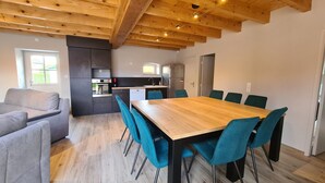 Una cocina moderna con techo de madera, un comedor con mesa de madera y sillas azul verdosas, y un sofá gris en la sala de estar.