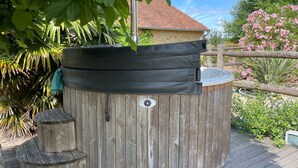 A wooden hot tub with a black cover, surrounded by lush greenery and a wooden deck. - Charming cottage near Le Mans with natural pool (Teloché)