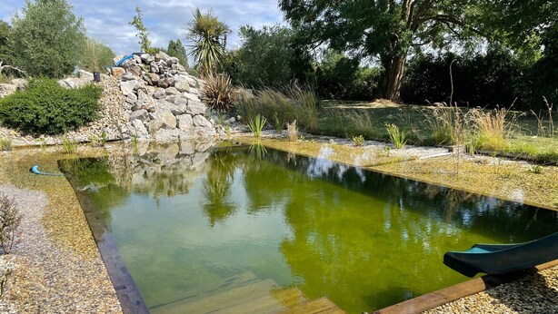 A rectangular pond with a wooden deck edge, surrounded by pebbles and various plants. - Charming cottage near Le Mans with natural pool (Teloché)