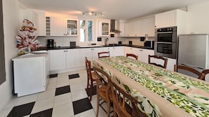 A modern kitchen with white cabinets, a black countertop, and a dining area with a table covered in a floral tablecloth. - Independent House with Garden in South Berry (Crozon-sur-Vauvre)