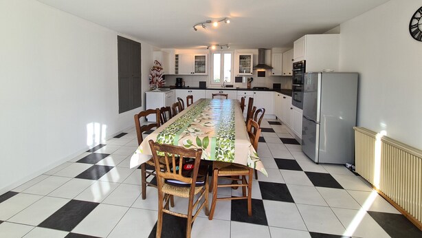 A spacious kitchen with a dining area, featuring a long table, chairs, and a clock on the wall. - Independent House with Garden in South Berry (Crozon-sur-Vauvre)
