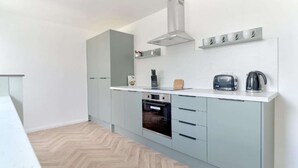 Une cuisine moderne avec des meubles gris, un four encastré, une bouilloire et un grille-pain.