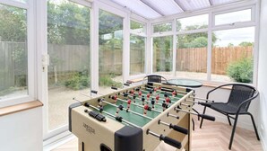 Une table de baby-foot dans une pièce baignée de lumière, avec de grandes fenêtres, une chaise et une table.