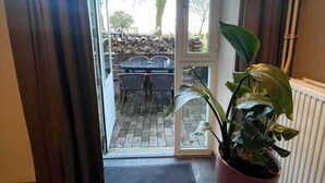 Ein Eingang führt zu einer Terrasse im Freien, mit Tisch, Stühlen, einem Blumentopf und einer Fußmatte.