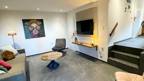 Ein modernes Wohnzimmer mit einer Couch, einem Couchtisch, einem an der Wand befestigten Fernseher und einer Treppe, die zu einer anderen Ebene führt.