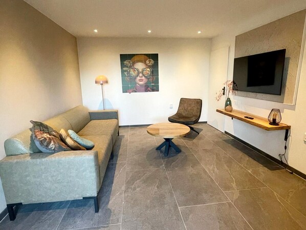 Ein modernes Wohnzimmer mit einer Couch, einem Sessel, einem Couchtisch, einem Fernseher und einem Bild an der Wand.