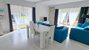 A modern living room with a dining area, featuring a white table and chairs, blue sofas, and a stone accent wall. - Mountain house in 24,000m² park. Pets allowed. (Aucun)