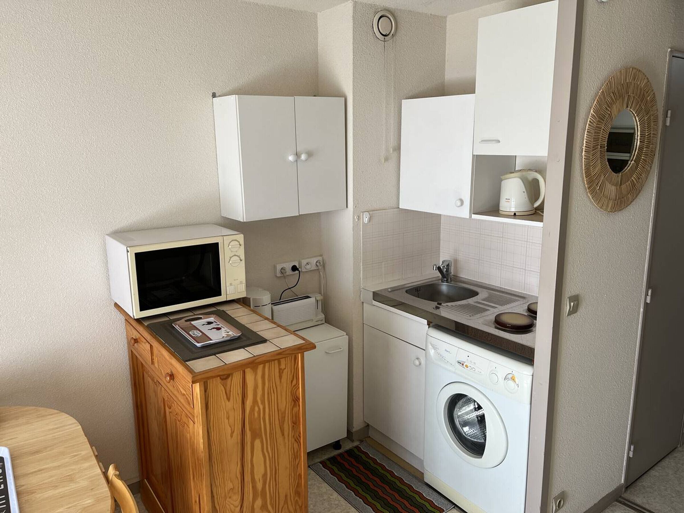 A compact kitchenette with a microwave, sink, and washing machine.