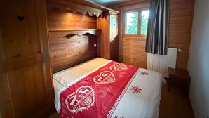 Een knus kamertje met houten wanden en een enkel bed met een rood-witte sprei.