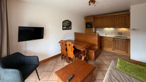 Een gezellig, compacte leefruimte met een televisie, houten eettafel, bank en kitchenette.