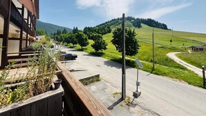 Un edificio con balcón, camino pavimentado y paisaje montañoso con árboles.