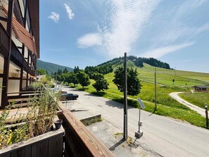 A building with a balcony, a paved road, and a hilly landscape with trees.