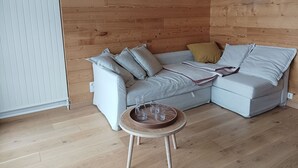 Una sala de estar moderna con un sofá seccional de color gris claro, una pequeña mesa redonda de madera con vasos, y paneles de madera en la pared.