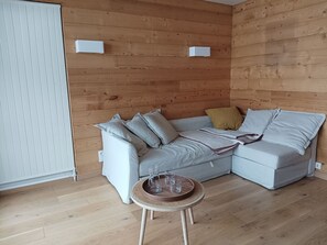 A modern living room with a light grey sectional sofa, a small round wooden table with glasses, and a wooden wall paneling. - Renovated apartment in the heart of Vercors in Autrans, up to 5 guests, sunny terrace (Autrans-Méaudre en Vercors-Autrans)