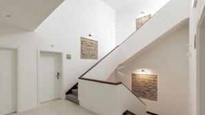 A modern staircase with a wooden handrail and white walls, leading to a landing with a stone accent wall. - Estúdios Loreto (Fuseta)