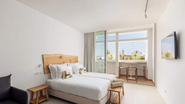 A modern hotel room with a large bed, a desk, and a view of the outside. - Estúdios Loreto (Fuseta)