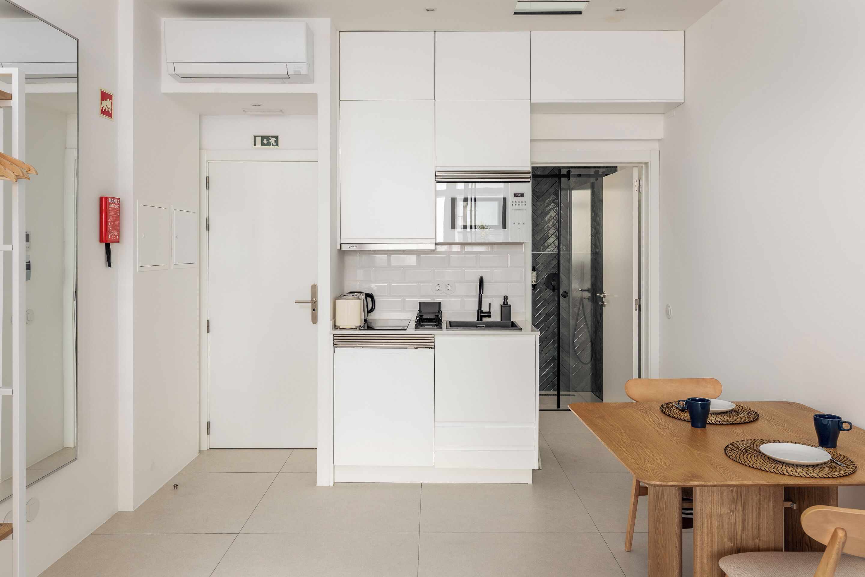 A modern kitchen with white cabinetry, a microwave, and a sink. There is a dining table with chairs and a small rug.