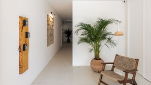 A hallway with a wooden wall art piece, a potted plant, a wicker chair, and a lamp. - Estúdios Loreto (Fuseta)
