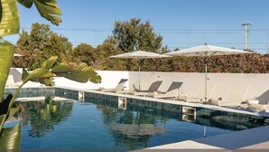 A swimming pool with lounge chairs and umbrellas, surrounded by a low wall and greenery. - Estúdios Loreto (Fuseta)