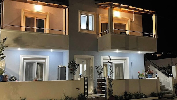 Un immeuble de deux étages doté d’un balcon à l’étage supérieur, d’une entrée sécurisée par un portail et de plantes en pot disposées autour de la base.