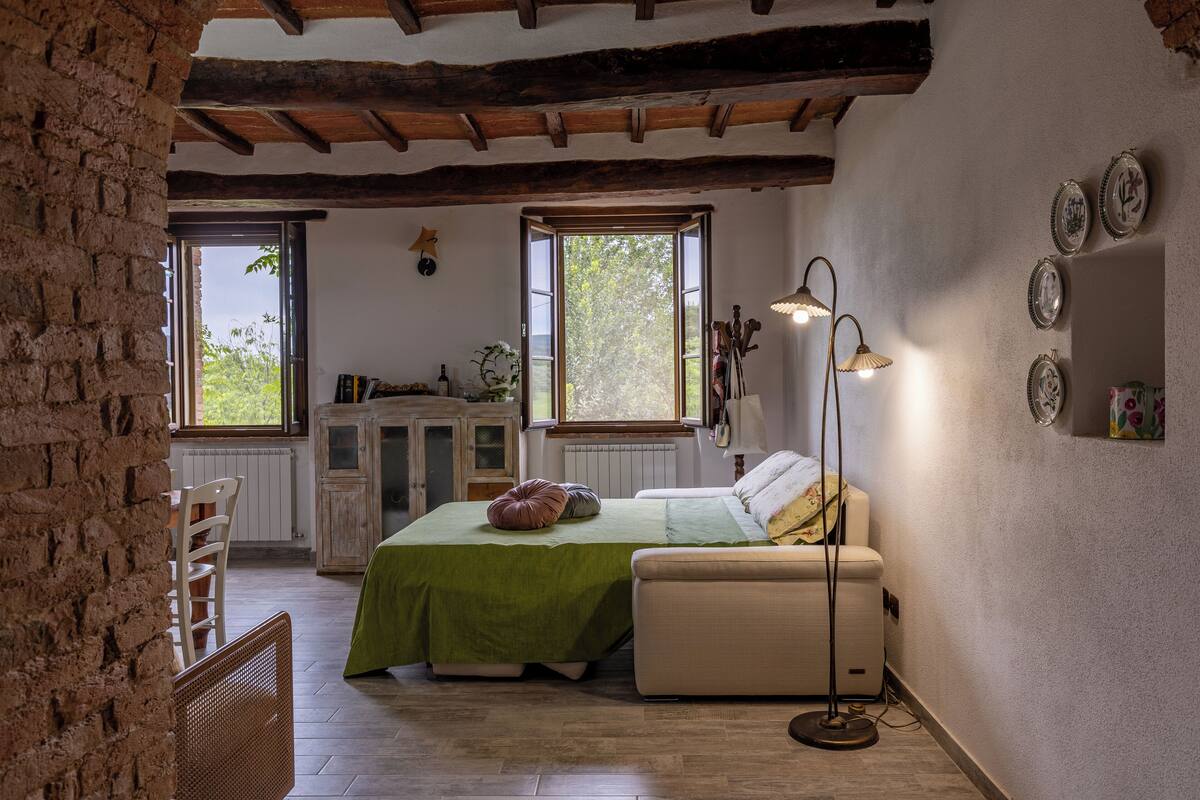 Une chambre à coucher au style rustique, avec une couvre-lit verte, un banc blanc et une lampe sur pied.
