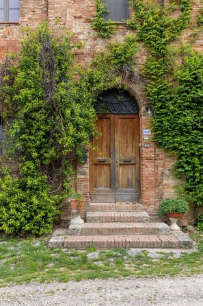 A brick building with a wooden double door, ivy-covered walls, and a small step leading to the entrance. - Pociano 1863 (Monteroni d'Arbia)