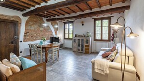 A rustic interior with exposed wooden beams, a brick wall, a dining area with wooden chairs, a sofa, and a cabinet. - Pociano 1863 (Monteroni d'Arbia)