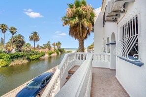 A balcony with a view of a river, palm trees, and a blue car parked on the side. - Apartment 'Chill Beach' with Shared Pool, Wi-Fi and Air Conditioning (Dénia)