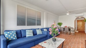 A living room with a blue sofa, a marble coffee table, and a dining area with chairs and a table.