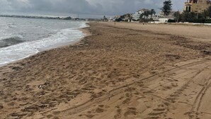 A sandy beach with footprints and a building in the background.