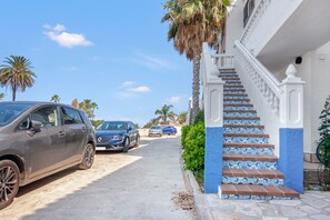 Una calle residencial con coches aparcados, una escalera con baldosas azules y blancas, y palmeras.