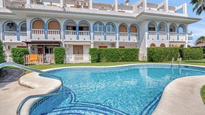 A large building with a swimming pool, multiple balconies, and a well-maintained garden.