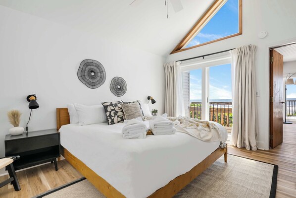 Ein Schlafzimmer mit einem großen Bett, einem Nachttisch, einem Schreibtisch und Blick ins Freie.