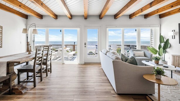 A spacious living area with a wooden ceiling, large windows, a sofa, a dining table, and chairs.