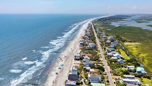 An aerial view of a coastal residential area with houses along the beach, a clear sky, and a calm sea.