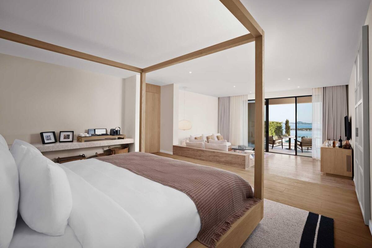 Una camera d'albergo moderna con un letto grande, un angolo salotto con divano e tavolo, un balcone con vista e una TV a parete.