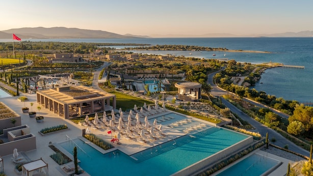 Un resort con una amplia piscina, varias zonas de descanso y vistas al mar.