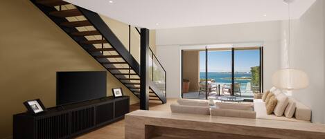 A modern living room with a staircase, a TV, a sofa, and a view of the sea.