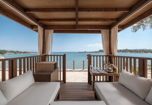 A wooden deck with a view of the sea, two sofas, a table with a drink, and a wooden railing. - Akra Didim Resort & SPA (Didim)