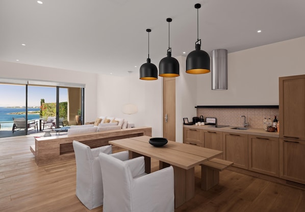 A modern kitchen with wooden cabinets, a dining area with white chairs, and pendant lights. - Akra Didim Resort & SPA (Didim)