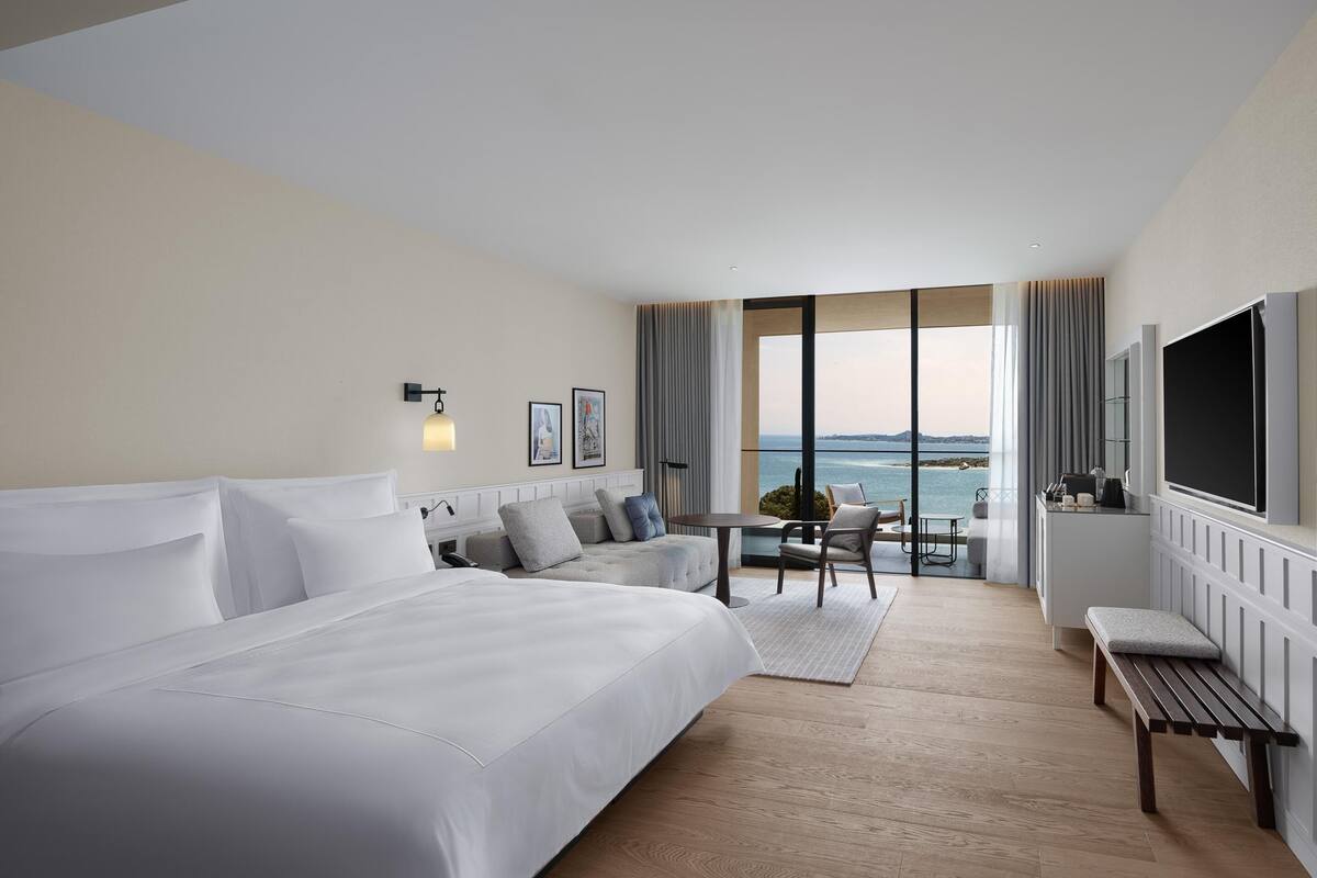 Una camera d'albergo moderna con un letto grande, un angolo salotto con vista e una televisione.