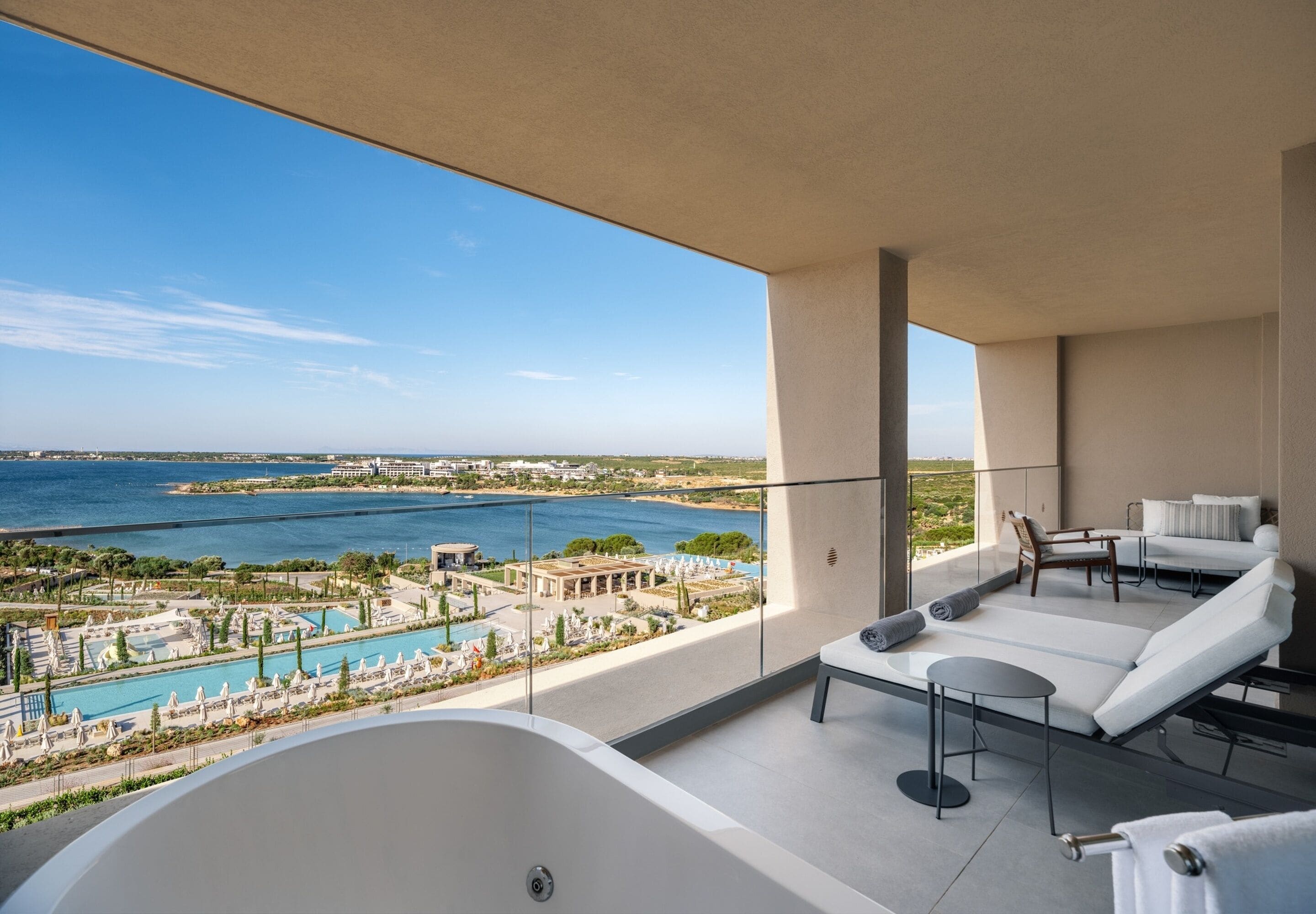 Un balcon avec vue sur la piscine et la mer, un jacuzzi et deux chaises longues.