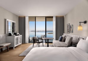 A modern hotel room with a large bed, a desk, a chair, a small table, and a view of the water. - Akra Didim Resort & SPA (Didim)