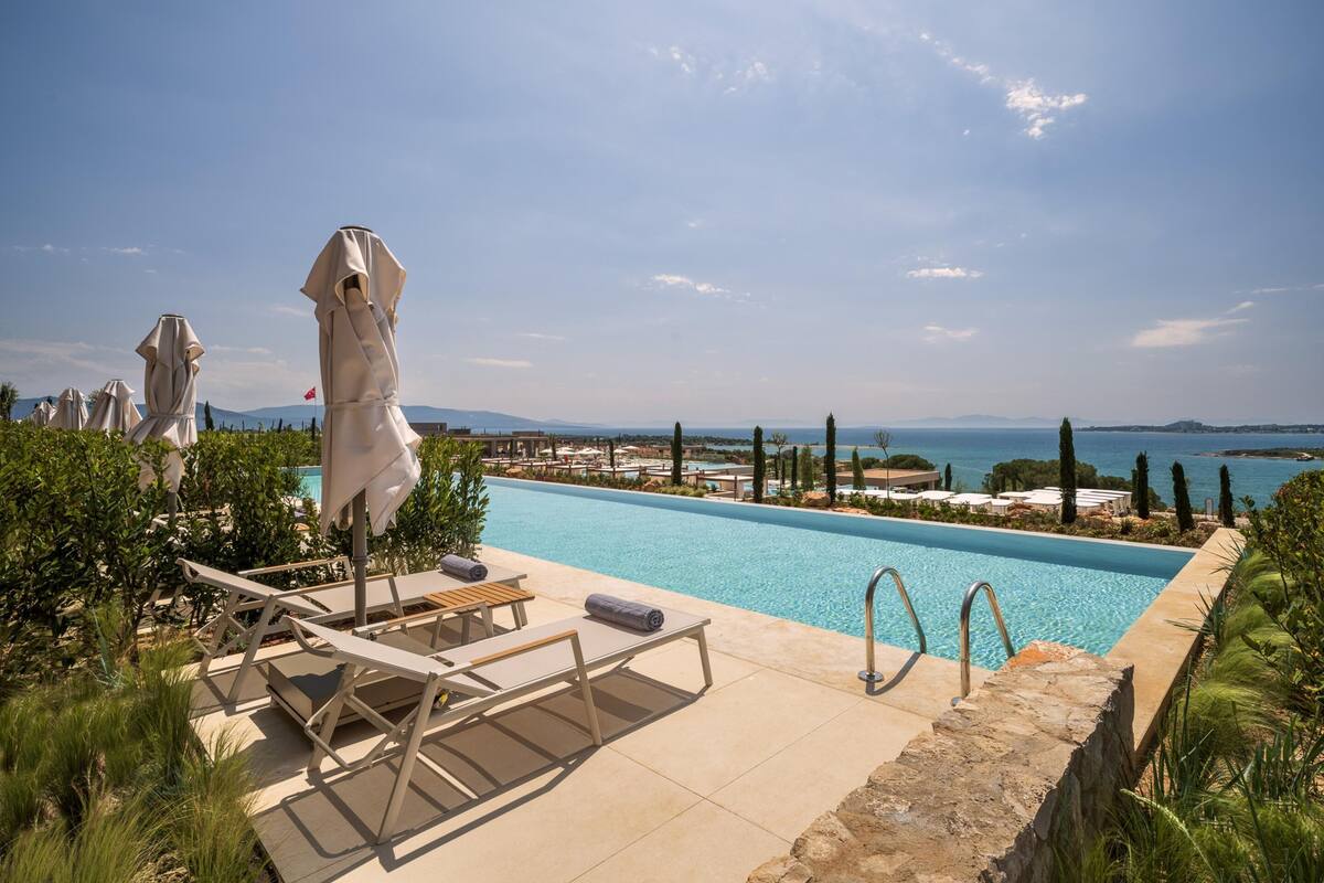 Una piscina con lettini e ombrelloni, immersa nel verde e affacciata sul mare.