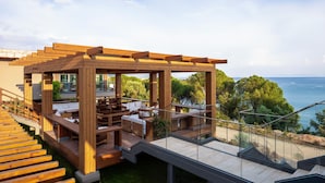 Una terraza moderna al aire libre con muebles de madera y barandas de vidrio que ofrece una vista panorámica del océano.