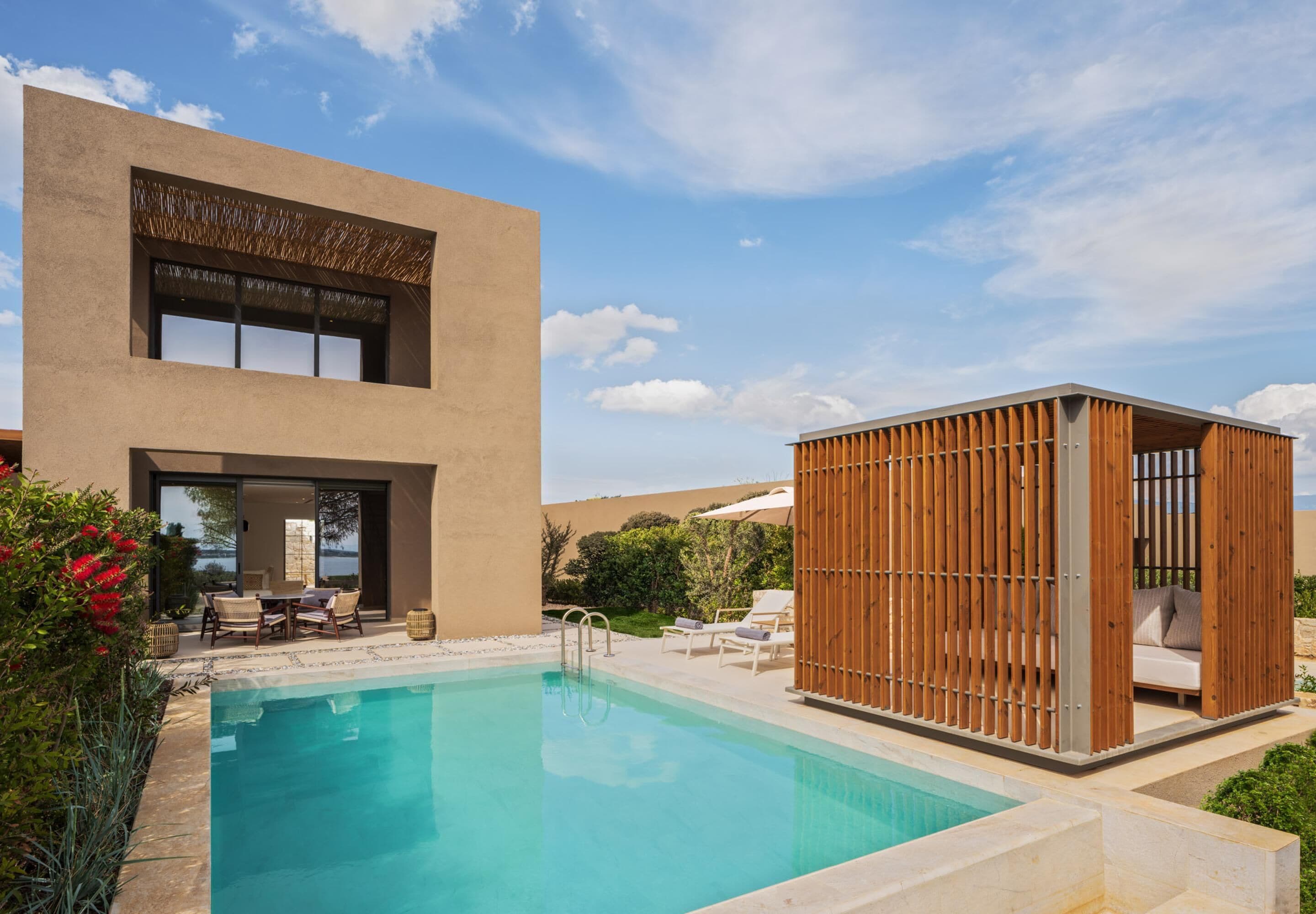 A modern pool area with a clear pool, lounge chairs, and a wooden cabana.