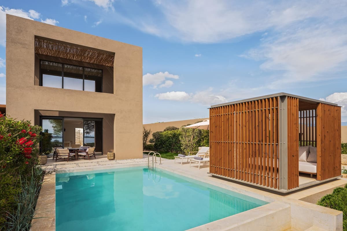 Un'area piscina moderna con piscina trasparente, sedie a sdraio e una cabana in legno.