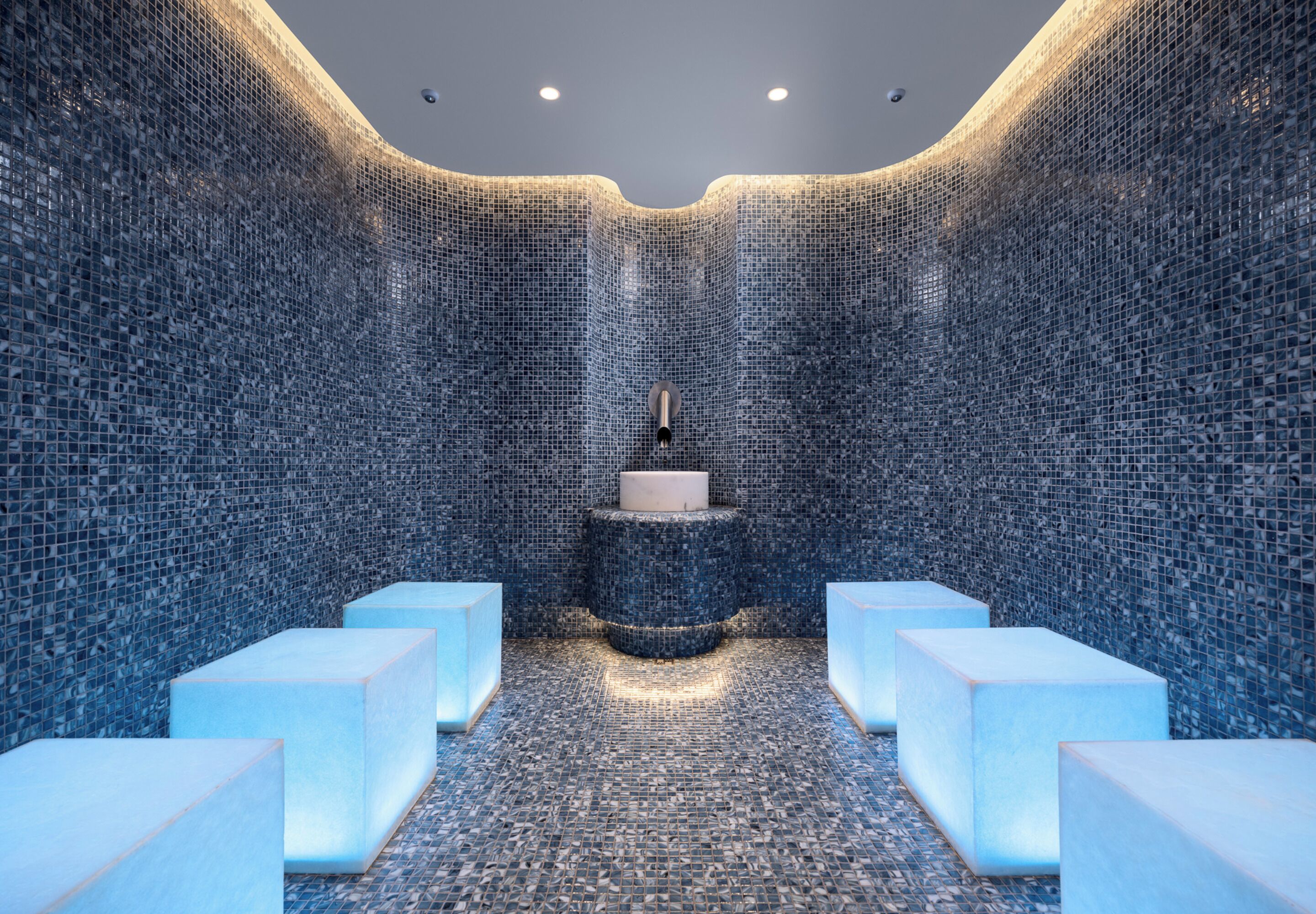 Un baño moderno con paredes de mosaico, un lavamanos central y zonas de estar.