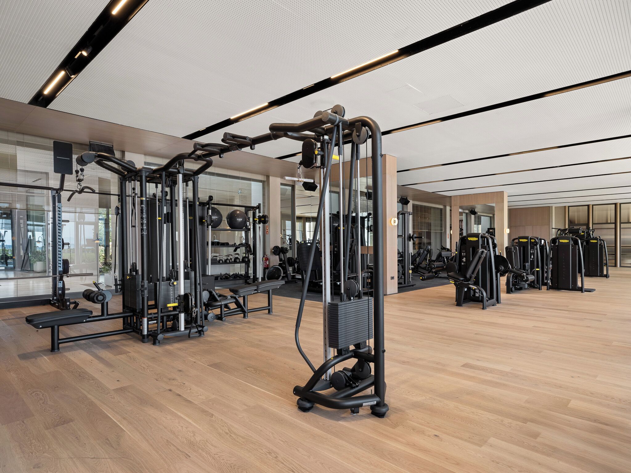 Een moderne sportschool met diverse trainingsapparaten, grote ramen en een houten vloer.